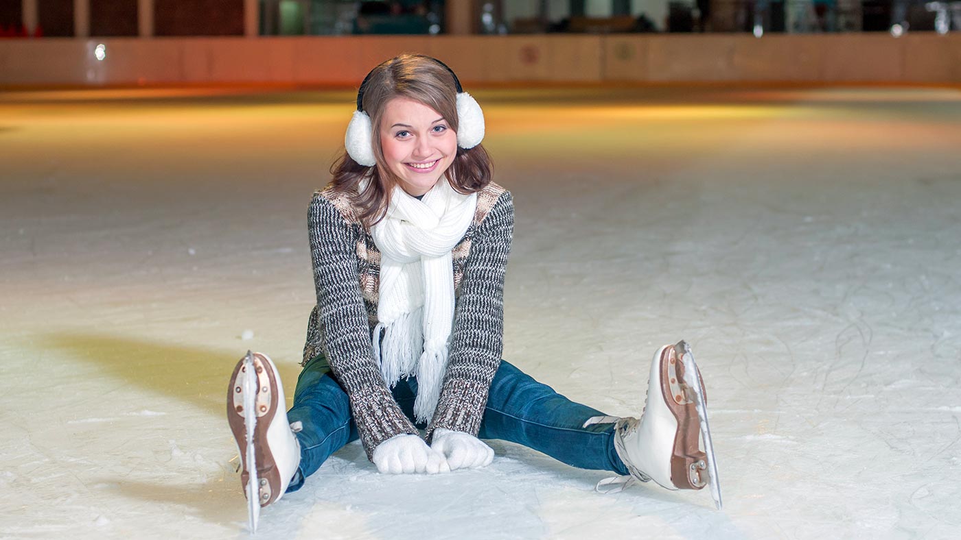 A girl sitting on a ice skating rink in Selva Val Gardena