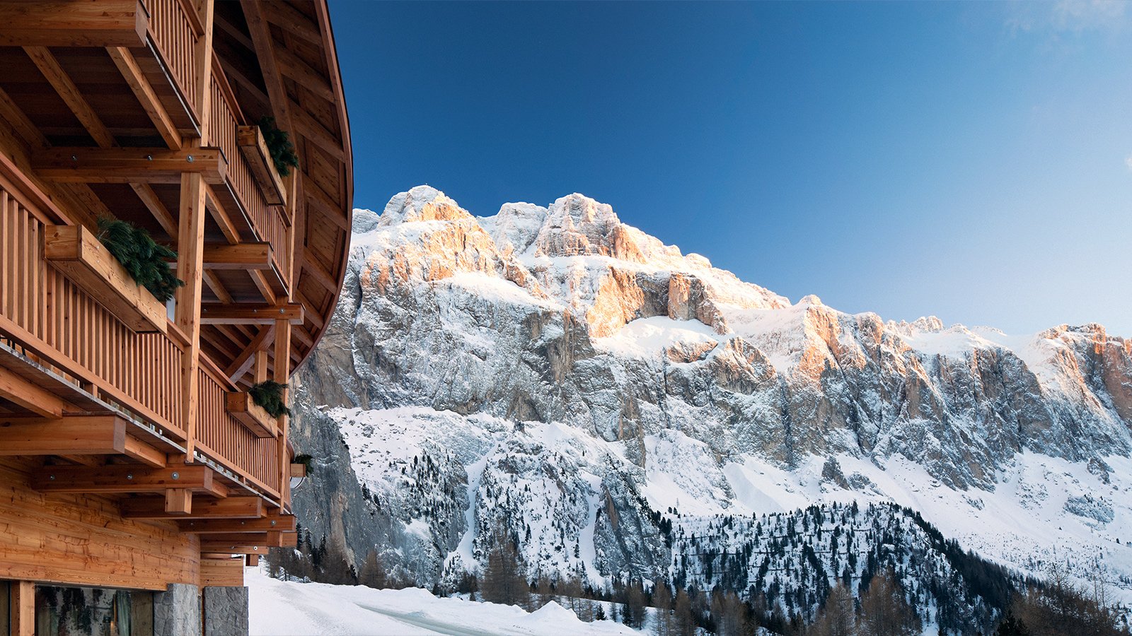Dettaglio del balcone in legno dello Chalet Gerard, con le imponenti pareti rocciose del Gruppo del Sella sullo sfondo