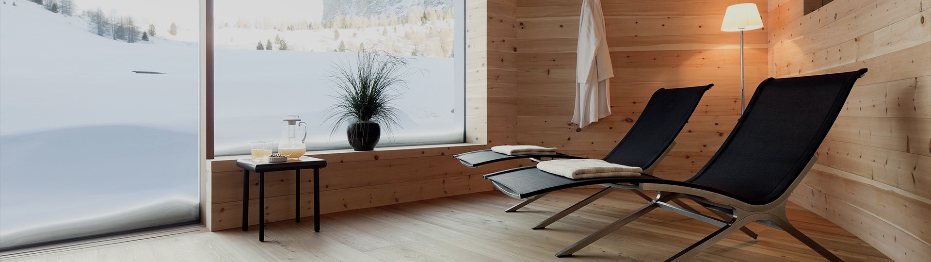 Relaxation area with wooden loungers and a panoramic view of the snowy landscape through a large window.
